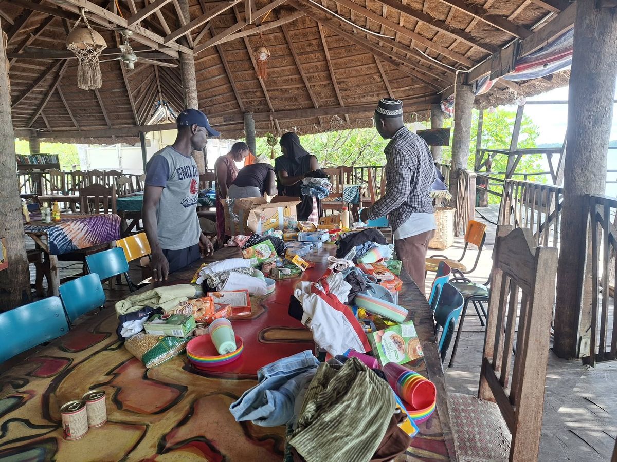 Volunteers sorting donated food, clothing and household goods on a long table in an open hall by the water