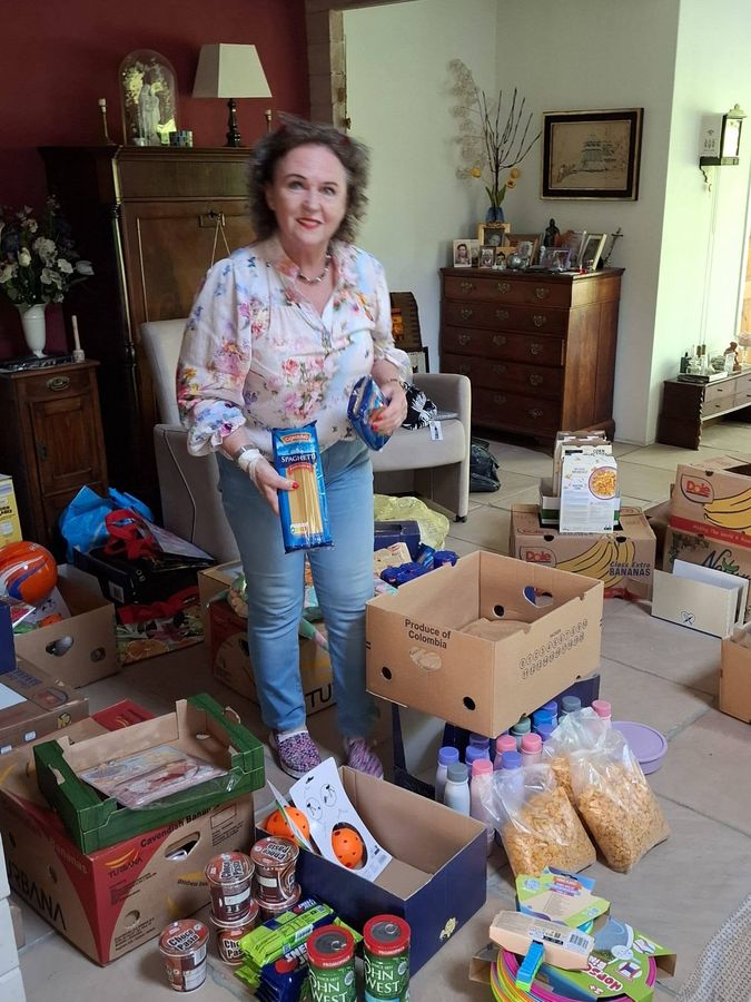 A supporter in the Netherlands standing among dozens of boxes packed with food, clothing and toys for The Gambia