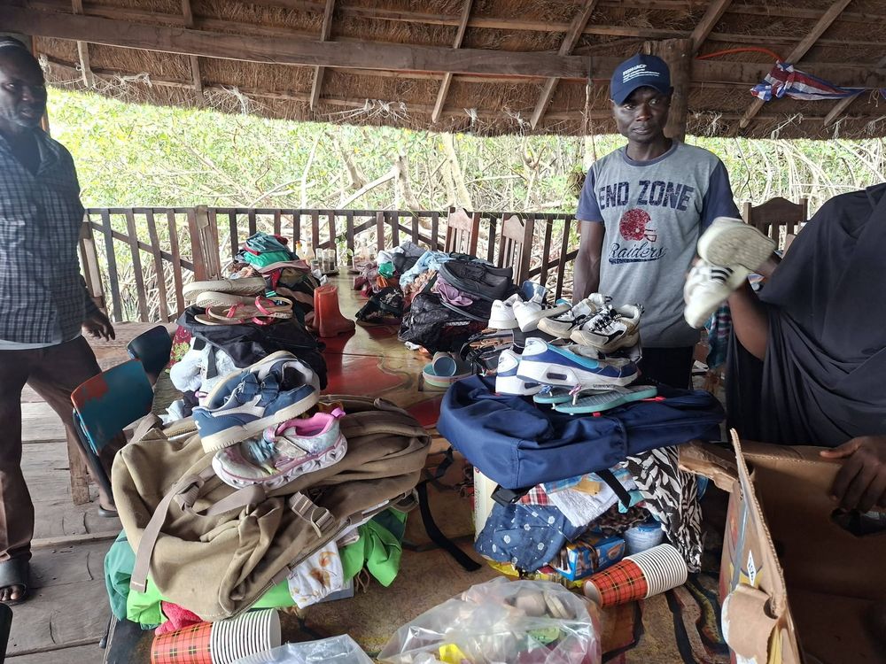 A volunteer holding up donated shoes beside tables of sorted clothing and bags